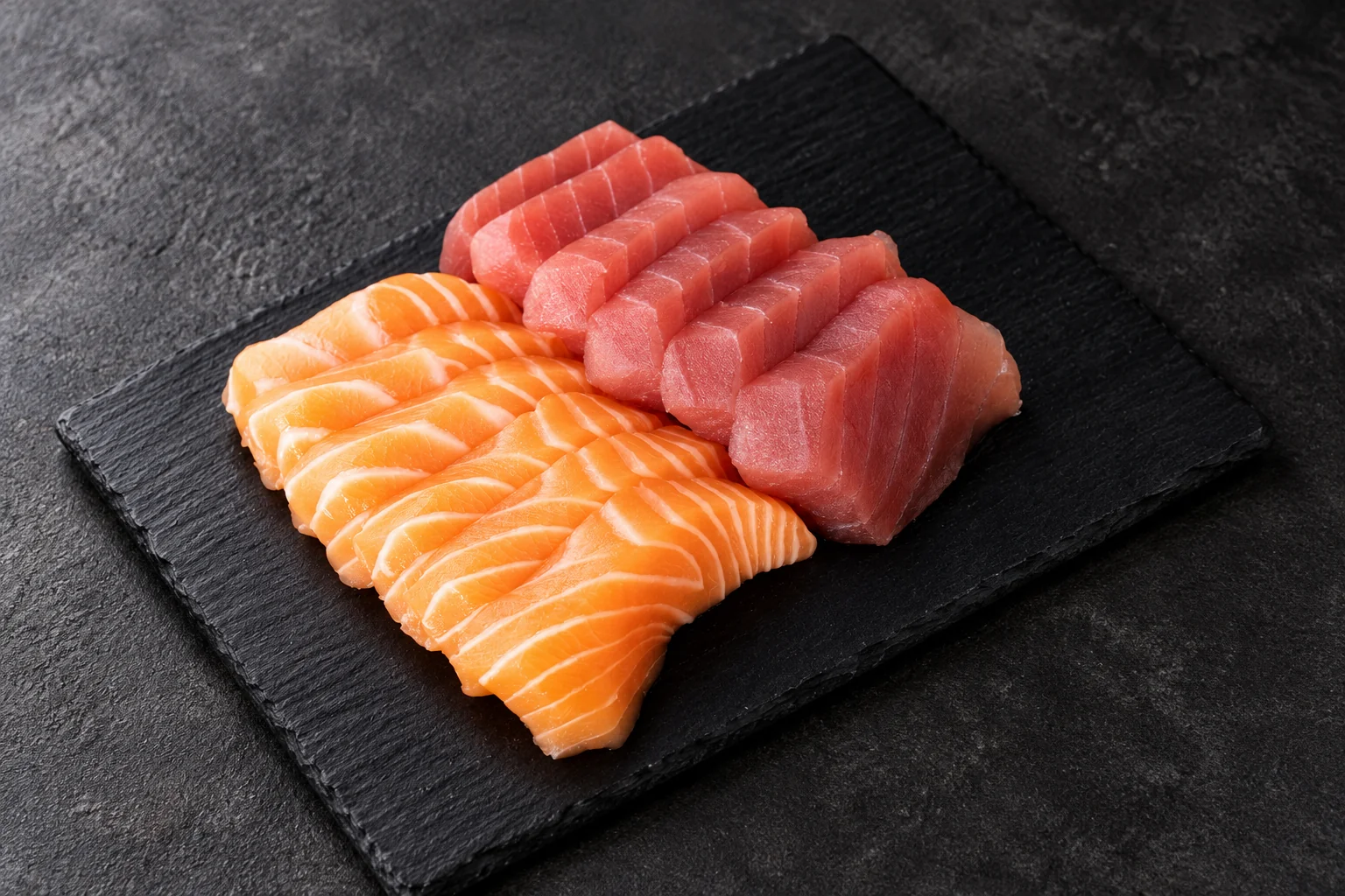 Salmon and tuna sashimi on a black slate, dark background.