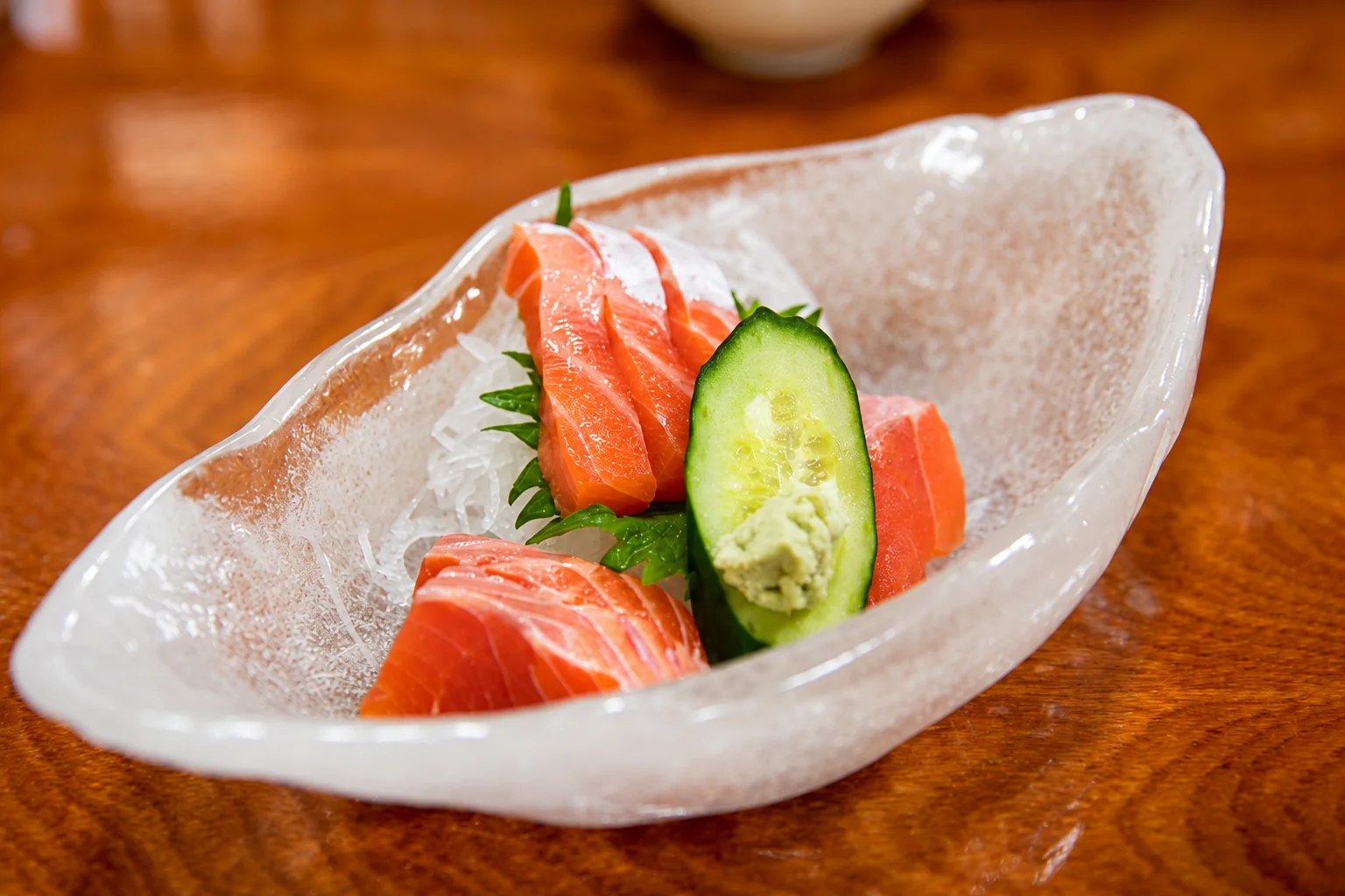 Salmon slices and cucumber in a glass dish, on a wooden table.